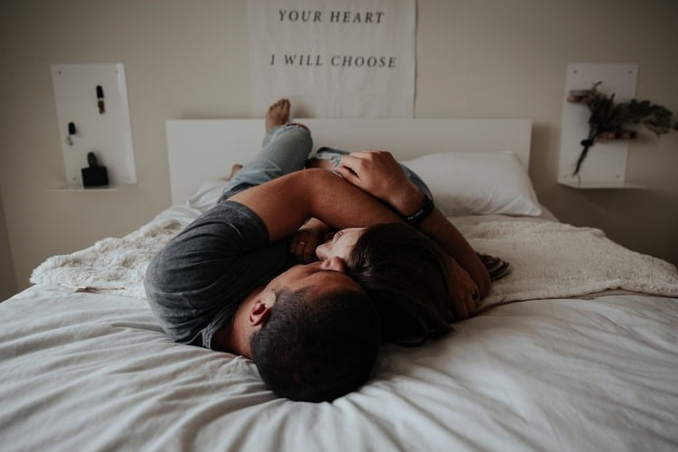 A couple holding each other while laying in bed together.