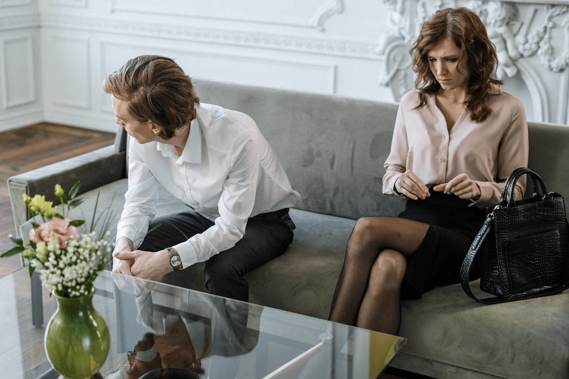 An upset married couple sitting on a couch in a counseling session with a therapist