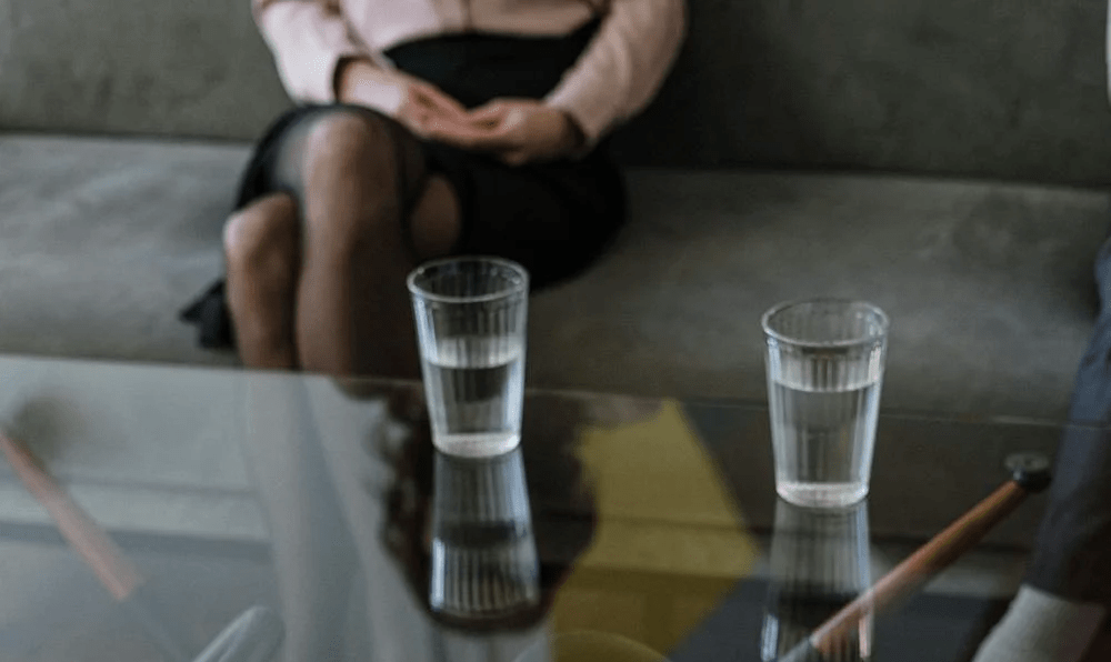 A glass-top table with two glasses of water between two individuals in a counseling session.